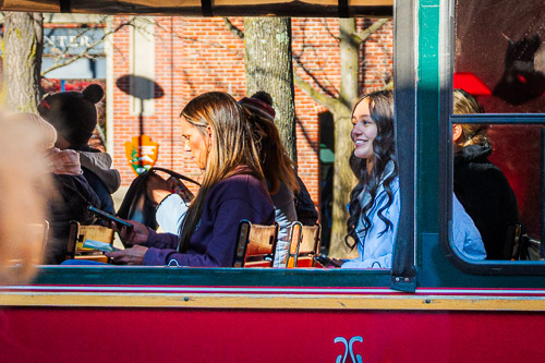 A young woman smiles at the camera from a trolley seat, surrounded by other passengers