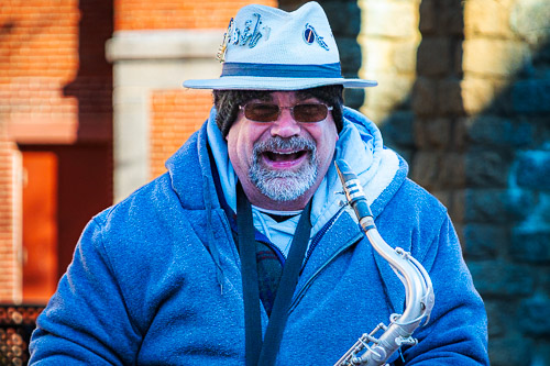 A street musician plays the saxophone near a sign that reads 