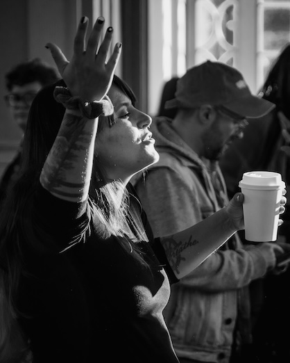 A smiling woman holds a coffee cup while standing in warm indoor light.