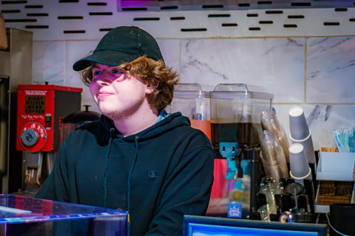 A cheerful barista smiles warmly behind the counter of a coffee shop.