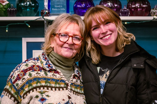 Two staff members smile behind the counter of Moody's Home & Gifts, surrounded by colorful glass pumpkins and decor.